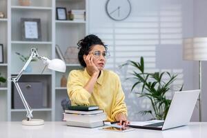 Overworked and overwhelmed woman studying remotely, hispanic woman upset sitting at desk inside home office, trying to learn online remotely. photo