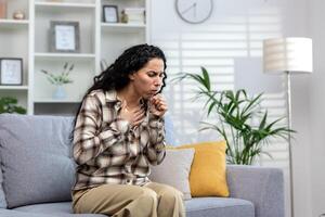 Woman having cold and sick coughing sitting on couch at home, hispanic woman in living room with cold and flu. photo