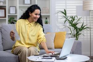 Smiling young beautiful woman reading banking paper notification about last mortgage payment while calculating budget at home. Happy hispanic girl feeling excited of good news in letter notice photo