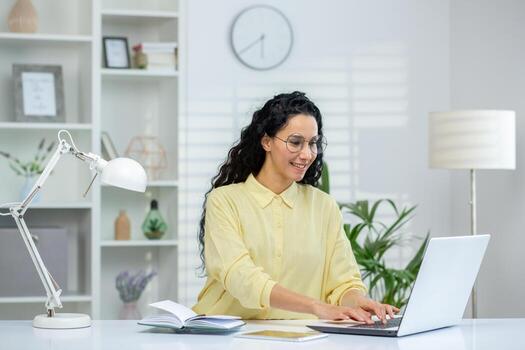 un alegre Hispano mujer es comprometido con su ordenador portátil en un bien iluminado y organizado hogar oficina, mostrando productividad y comodidad. foto