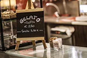 masi Italia 7 7 junio 2023 un cerca arriba foto de un pequeño pizarra firmar mostrando helado precios en italiano en un bar mostrador