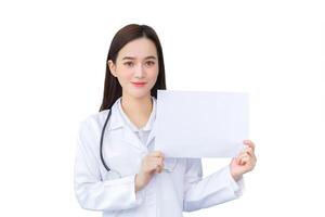 Young asian professional woman doctor who wears medical coat holds and shows white paper to present something in healthcare concept while isolated white background. photo