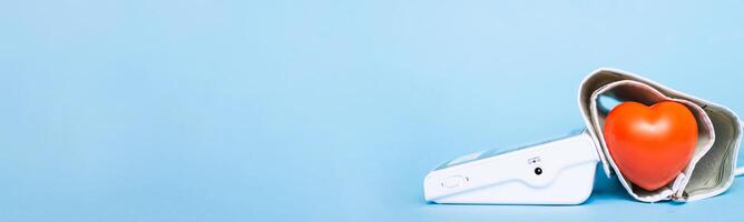 Red heart and white electronic tonometer isolated on a blue background photo