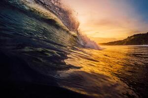 Perfect barrel wave crashing in tropical ocean with warm sunset tones. photo