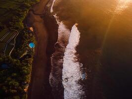 Aerial view of black sand beach with sunrise or sunset tones and ocean with waves in Bali photo