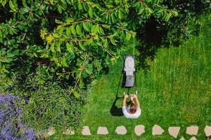 Man pushing lawn mower for cutting green grass in garden with sunlight at summer. Aerial view. photo