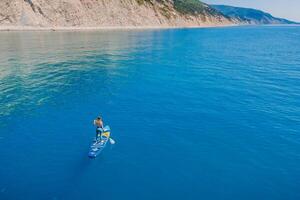 July 15, 2021. Anapa, Russia. Sporty woman on stand up paddle board at blue sea. Surfer woman walking on Gladiator SUP board in sea. Aerial view photo