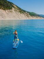 May 20, 2022. Dalaman, Turkey. Sporty woman on stand up paddle board in blue sea. Surfer girl walking on Gladiator SUP board in sea. Aerial view photo