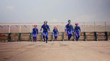 Group of skydivers running excitedly on a landing field, wearing blue jumpsuits and parachutes video