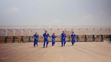 grupo de trabajadores en azul uniformes bailando en frente de un grande industrial invernadero. video