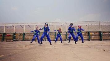 grupo de trabajadores en azul uniformes alegremente bailando en un hormigón superficie con un claro cielo en el antecedentes. video