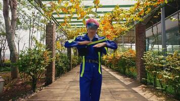 Stylish person with colorful hair wearing a blue jumpsuit and sunglasses dancing in a lush greenhouse. video
