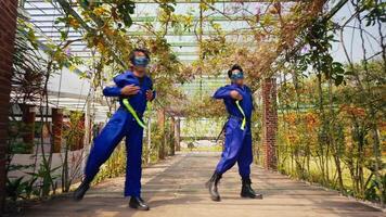 Two people in blue overalls posing in an urban garden with brick columns and greenery. video