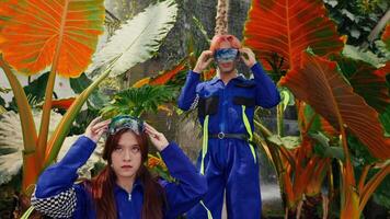 dois pessoas dentro vibrante fantasias com óculos no meio tropical folhagem, retratando futurista exploradores video