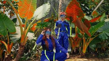 dos personas en vibrante disfraces con gafas de protección en medio de tropical follaje, retratar futurista exploradores video