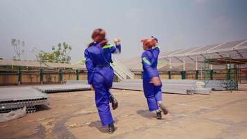 Two women in blue jumpsuits dancing confidently at an industrial site. video