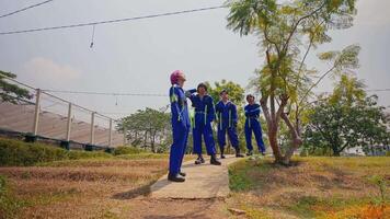 Workers in blue uniforms walking on a path with trees and power lines in the background on a sunny day. video