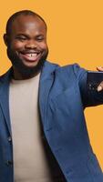 Vertical Joyous man using smartphone to take selfies and post them on social media. Happy BIPOC person taking photos using phone selfie camera, isolated over yellow studio background, camera A video
