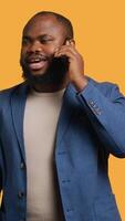 Vertical Joyous man with positive emotion, enjoying talking with friends phone call using smartphone, studio background. Happy african american person with smile on face during telephone call, camera A video