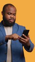 Vertical Upbeat man having friendly conversation with friends during teleconference meeting using smartphone, studio background. BIPOC person has fun catching up with mates during online call, camera A video