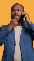 Vertical African american man having thoughtful conversation with friend during telephone call, studio background. Pensive BIPOC person talking on phone with mate, doing thinking gesturing, camera A video