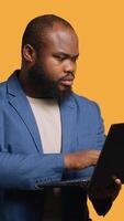 Vertical African american man using laptop to do business related tasks for company, isolated over studio background. Office clerk doing budgeting, forecasting, and financial analysis on notebook, camera A video