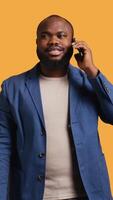 Vertical Joyous man with positive emotion, enjoying talking with friends phone call using smartphone, studio background. Happy african american person with smile on face during telephone call, camera B video