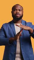 Vertical Portrait of assertive BIPOC man asking for timeout, doing hand gestures, feeling fatigued. Unhappy person doing vehement pause sign gesturing, wishing for break, studio background, camera B video