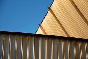 Urban Close-up photography Architectural elements of Exterior made of Brass Rails. Golden Fluted Facades shimmer in Sun against the Blue Sky. Yellow edges Cling Sunlight. Background brighter in blur photo