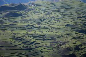 inspirador aéreo agricultura paisaje de aterrazado campos y jardines en un soleado día. cultivo de tierra en pueblos alto en el montañas. oscuridad de nubes otoño en el prados fuera de el ciudad foto