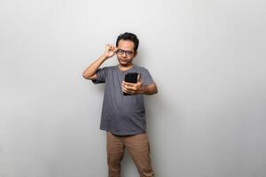 a handsome Asian man in gray is looking at a smartphone while adjusting his glasses with copy space photo