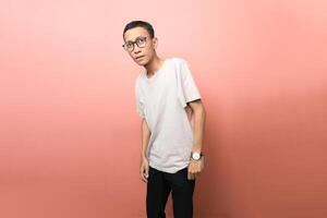 an Asian man wearing a plain white t-shirt with glasses with a surprised face isolated on red background photo