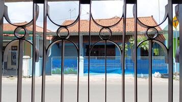 a simple house visible from a gap in an iron fence photo