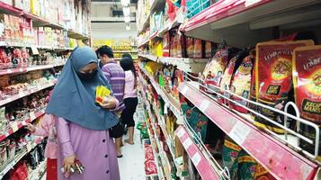 Semarang, Indonesia - May 8, 2024 - People at supermarket. Consumers visiting grocery store, shopping, Buyers, customers, Wearing Hijab. Trade and Consumerism photo