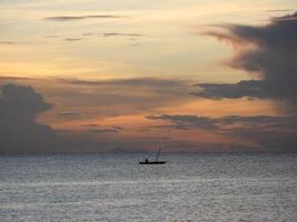 silueta de un solitario pescador en un barco a puesta de sol apagado el costa de Zanzíbar, Tanzania foto