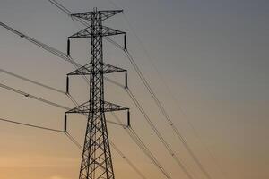 High voltage pole with many wires It was a silhouette with an orange sky as the background. photo