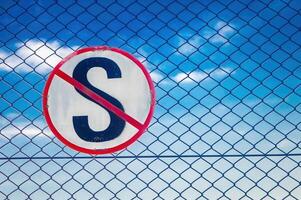 The no stopping sign here is in the shape of the letter S crossed out attached to an iron net photo