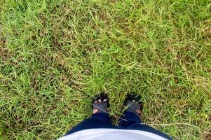 the point of view of a man or woman looking down at the sandals standing on the grass for background and copy space photo