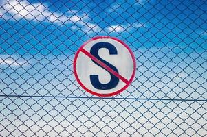 The no stopping sign here is in the shape of the letter S crossed out attached to an iron net photo