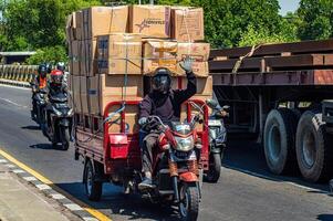 a person riding a tricycle on a pick-up motorbike carrying a pile of cardboard boxes containing shipping logistics, Indonesia, 16 May 2024. photo
