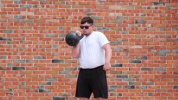 sports and leisure. strong Caucasian man working out using kettlebell in the park, brick wall background video