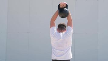 Esportes e lazer. Forte caucasiano homem trabalhando Fora usando kettlebell dentro a parque, branco parede fundo video