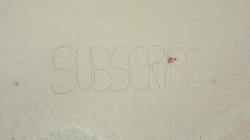 Aerial view of woman writing big text 'SUBSCRIBE' on white sandy tropical beach video