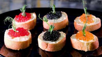 The camera slowly zooms in on the black plate for a close-up of the snack.. Sandwiches with red and black caviar on white bread video