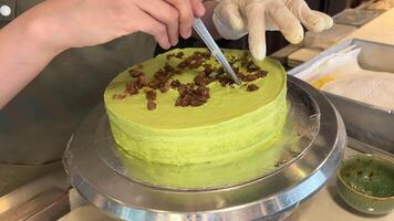 verde crema cucinando pistacchio torta diffusione con crema nel un' professionale cucina nel un' ristorante Aperto Schermo Astuccio appena preparato decorare con cioccolato e secco frutta video