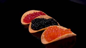 Sandwiches with butter and black caviar on black background, macro shoot. Morning breakfast with bread slices and red and black salty with boiled egg caviar on wooden table background. video