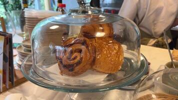 cuerno en mostrar. escaparate en un Tienda en un restaurante. croissants bollos con amapola semillas canelas debajo un vaso cubrir video