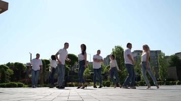 energie liefde leven. glad sexy Latijns dans beweegt. geënsceneerd dans bachata een groep van mensen dansen Aan de straat de dezelfde bewegingen wit overhemden blauw jeans volwassenen en jong mensen van verschillend leeftijden video