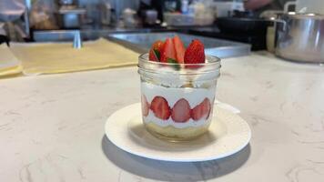 el camarero sirve dulces Leche postre con fresas de cerca ver de vaso cuenco con vainilla hielo crema y rojo fresa jarabe soportes en mesa. suave enfocar. postre tema. video