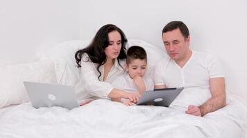 husband wife and son spend time together in bed holiday look at tablet communicate conversation love at home happiness joy success in gadgets white background place for advertising text happy family video